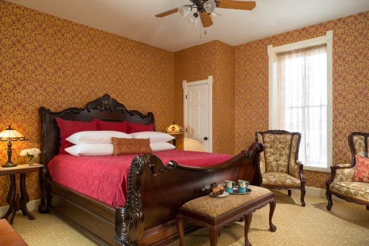 A cozy bedroom featuring a large ornate bed, patterned wallpaper, and vintage furniture.