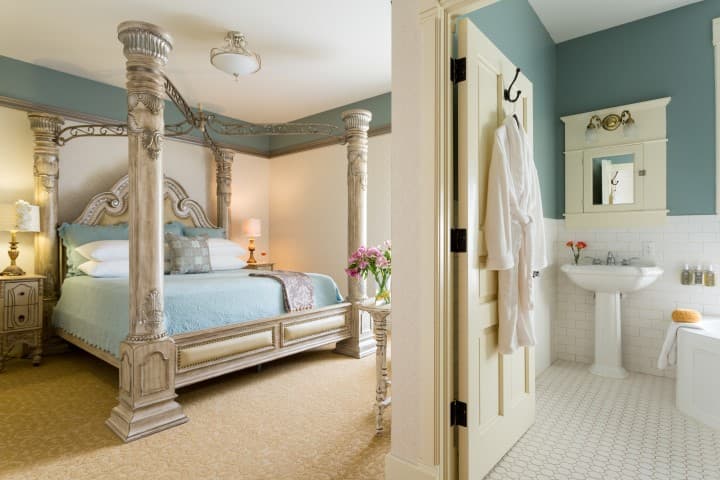 A cozy bedroom with a four-poster bed and an adjoining bathroom featuring white tiles and modern fixtures.