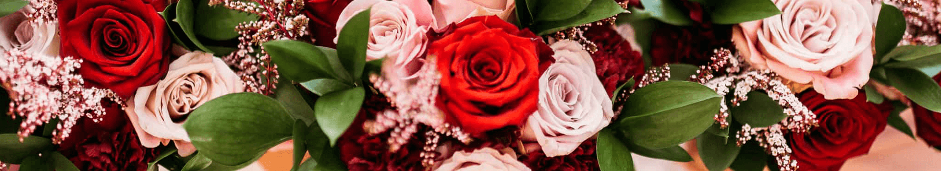 A vibrant arrangement of red and pink roses surrounded by lush green leaves.