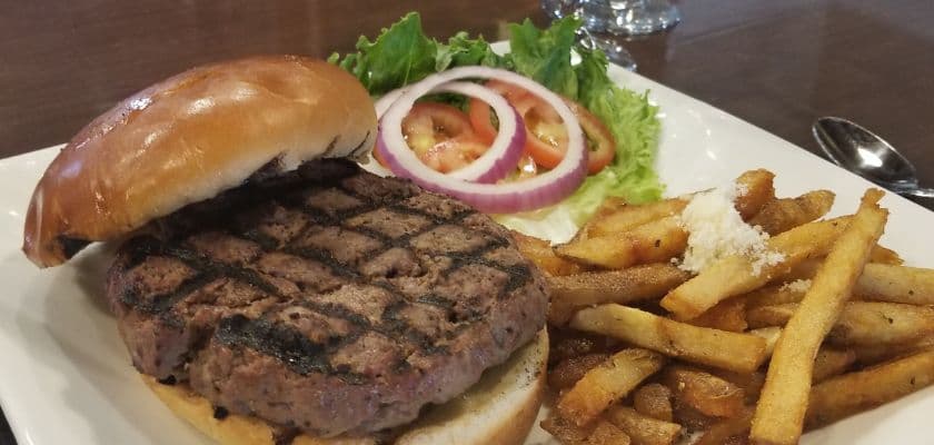 A grilled hamburger with lettuce, tomato, and onion on a bun, accompanied by a serving of French fries.
