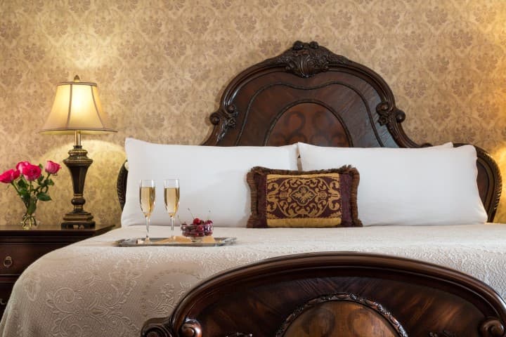 Elegant bedroom with a vintage bed, decorative pillows, two champagne glasses, and flowers.