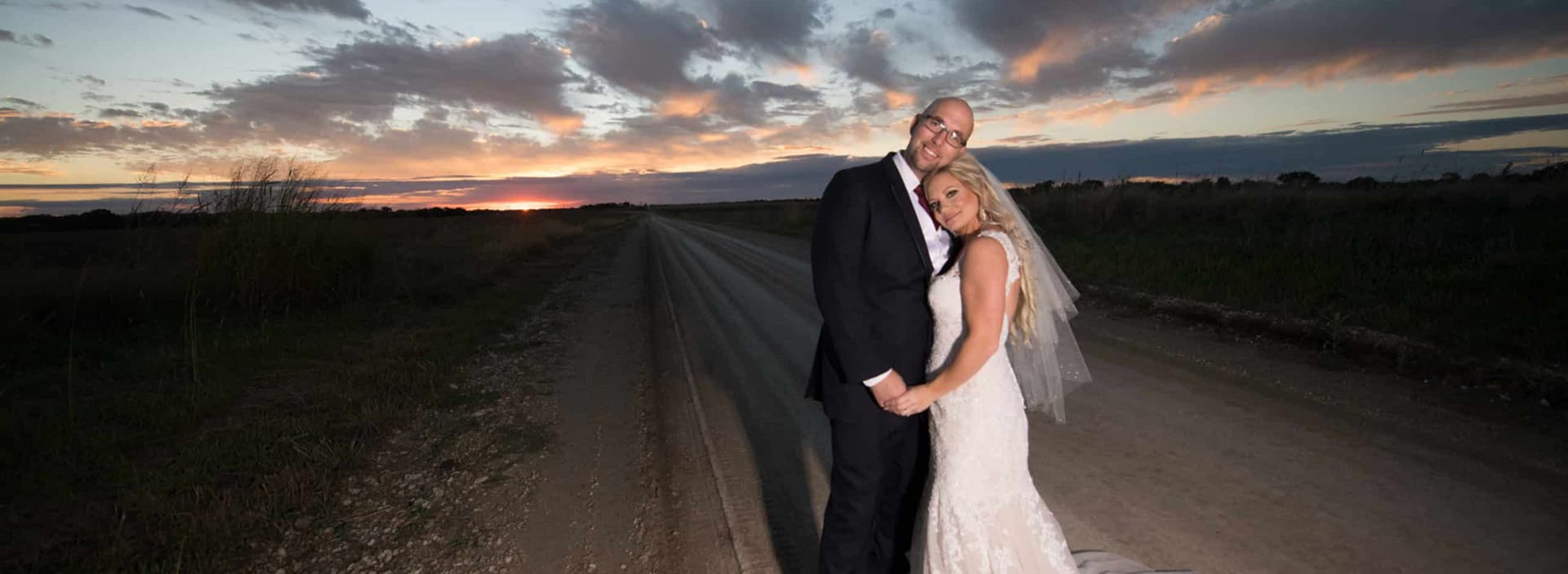 A happy couple poses together on a road at sunset, celebrating their wedding.