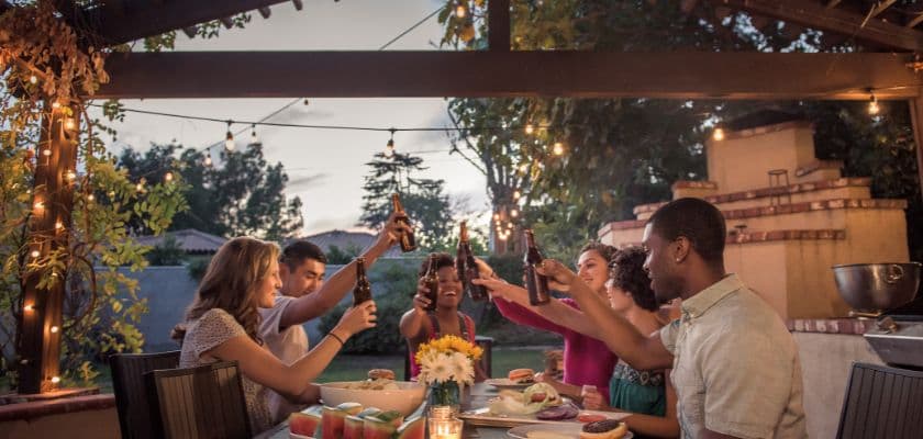 A group of friends toasts around a dinner table adorned with food and candles in a cozy outdoor setting.