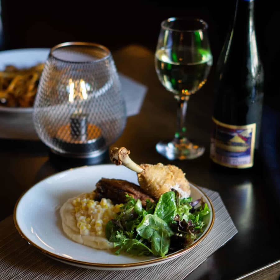A plate with fried chicken, mashed corn, salad, and a glass of wine beside a candle.