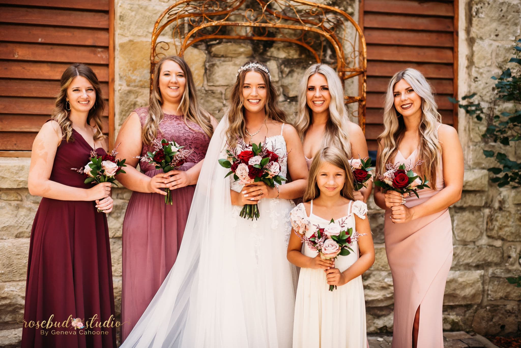 A bride and her bridesmaids pose together, holding bouquets, in a picturesque outdoor setting.