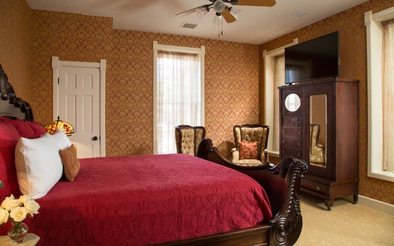 Cozy bedroom featuring a red bedspread, vintage furniture, and floral wallpaper.