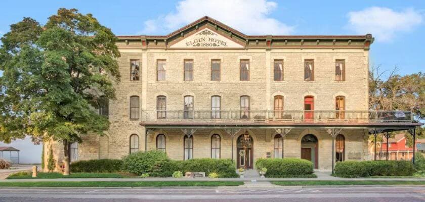 Historic brick hotel building with a decorative roof and balcony, surrounded by greenery.