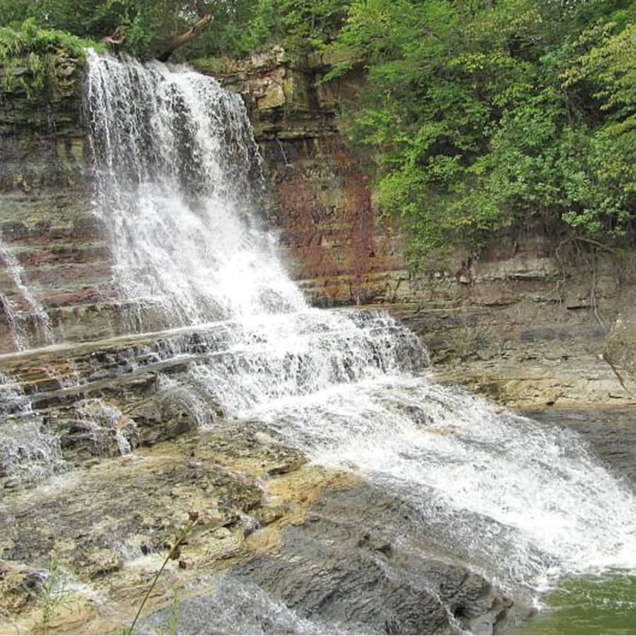 A cascading waterfall flows over rocky layers surrounded by lush greenery.