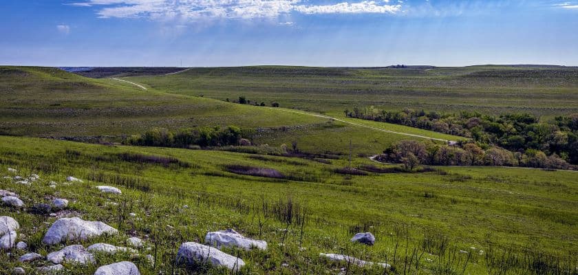 A panoramic view of rolling green hills dotted with white rocks under a bright blue sky.