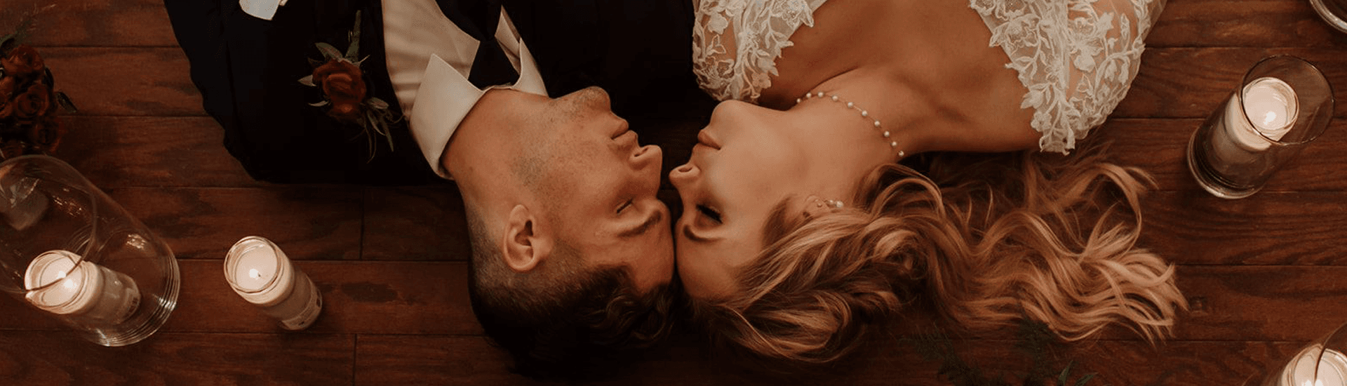 A romantic couple lies on the floor surrounded by candles and roses.