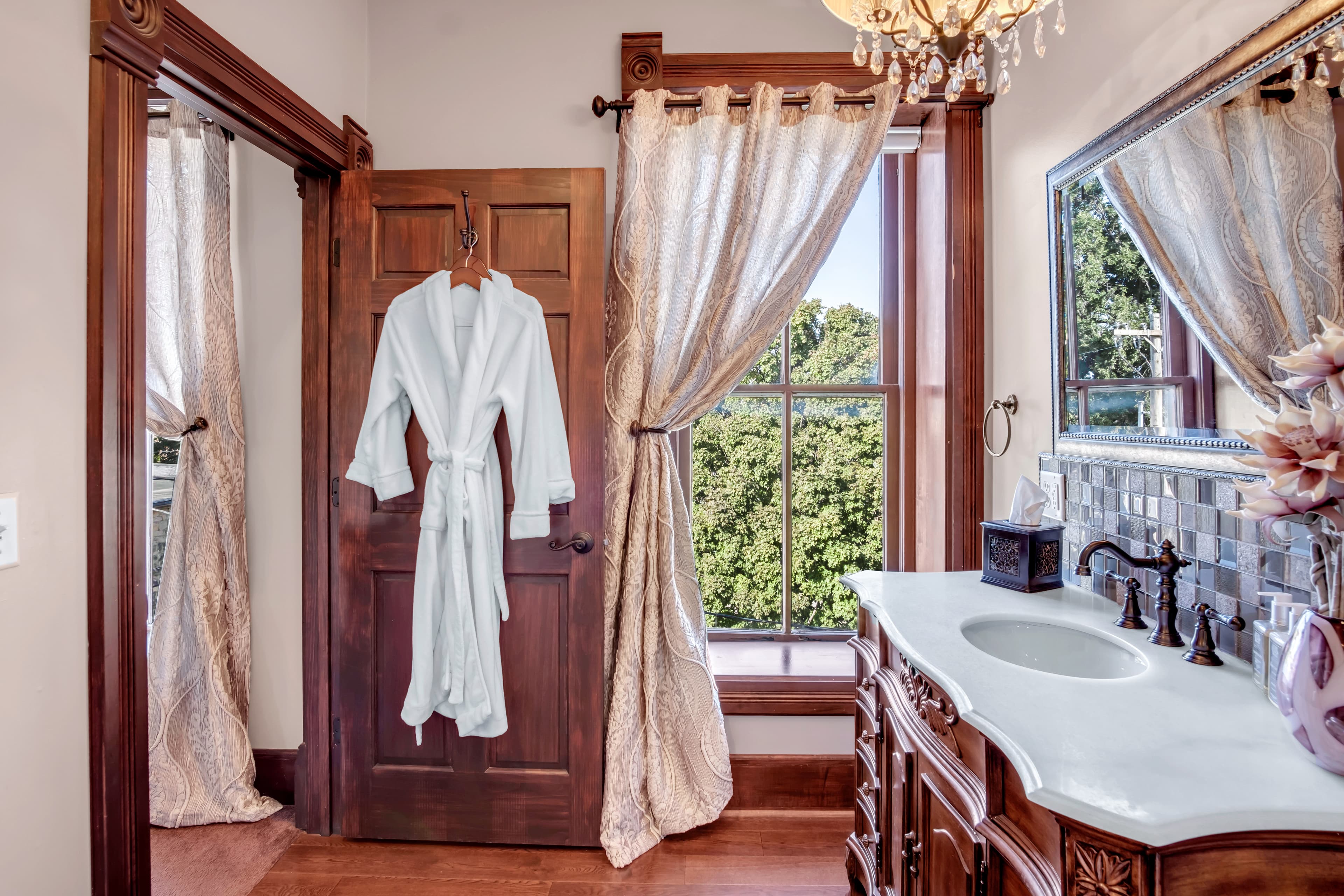 A stylish bathroom featuring a wooden door, hanging robe, elegant curtains, and a vanity with a sink.