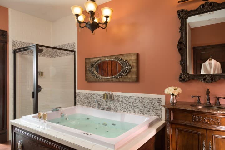 Elegant bathroom featuring a jetted tub, a glass shower, and a vintage-style mirror against a warm, peach-colored wall.
