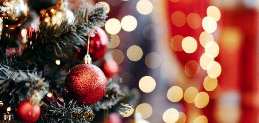 A close-up of a decorated Christmas tree with red ornaments and soft, blurred lights in the background.