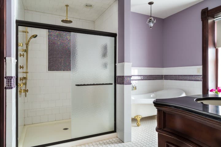 A modern bathroom featuring a glass shower, a freestanding bathtub, and purple accent walls.