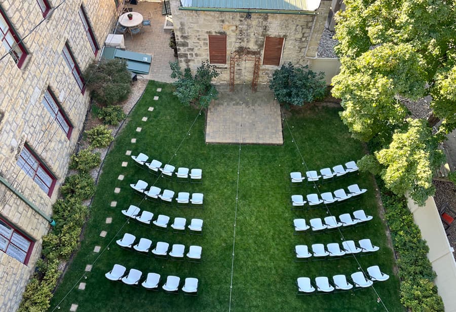 An aerial view of a grassy courtyard with white lounge chairs arranged in rows facing a stone structure.