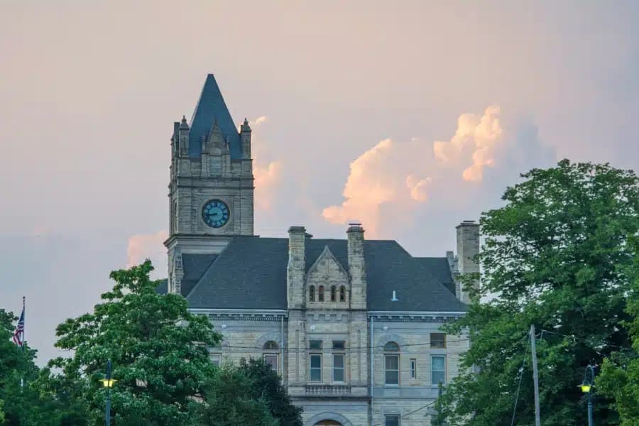 Historic clock tower of a stone courthouse against a pastel sky.