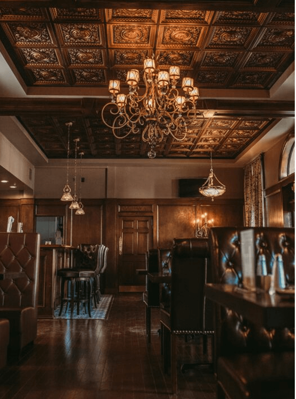 Elegant interior of a restaurant featuring ornate ceiling tiles and a chandelier.