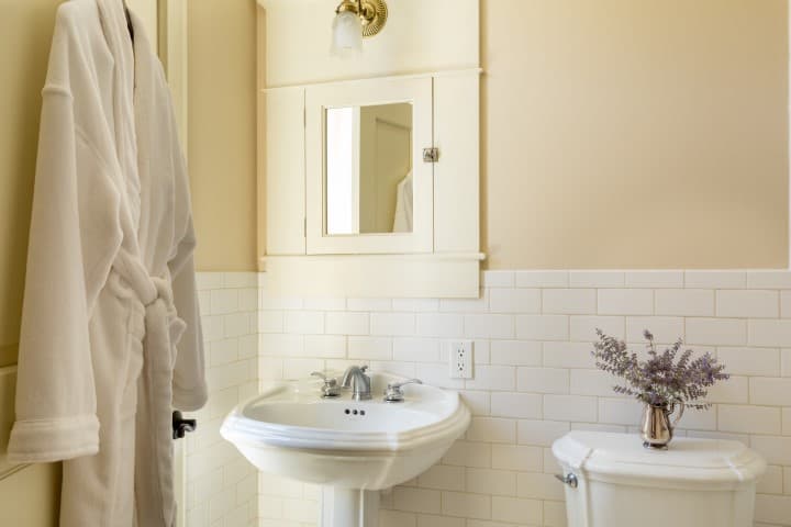 A cozy bathroom featuring a white robe, a vanity sink, a mirror cabinet, and a vase of lavender.