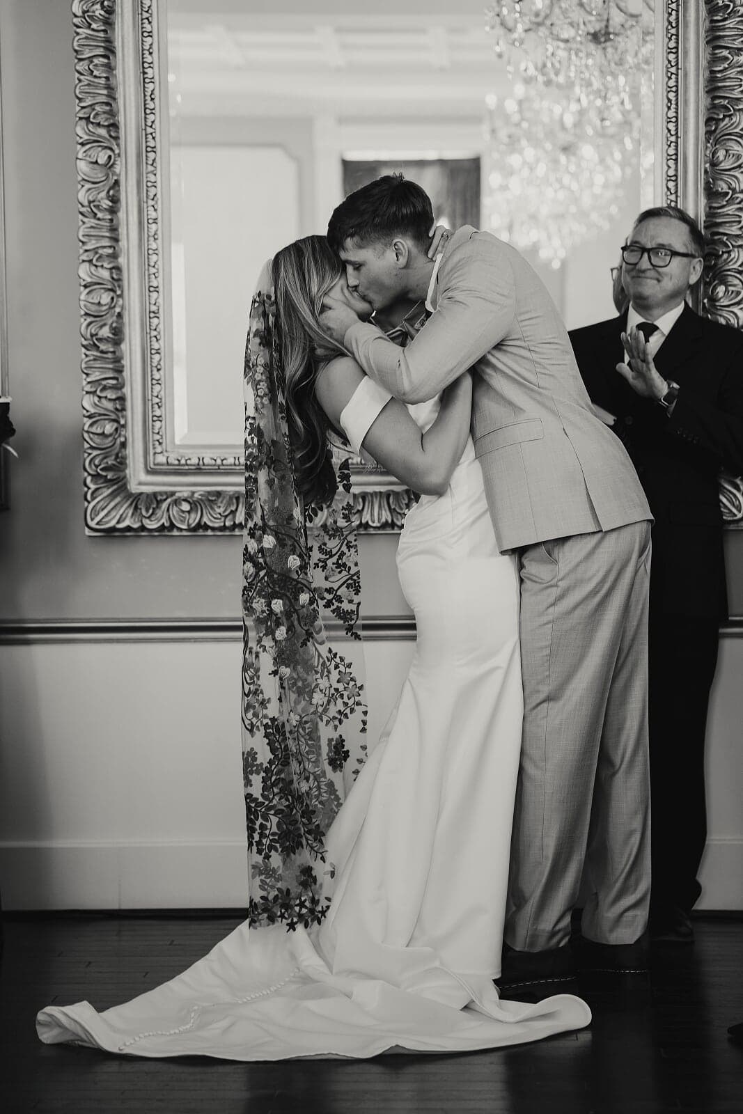 A couple passionately kisses during their wedding ceremony, while an officiant smiles in the background.