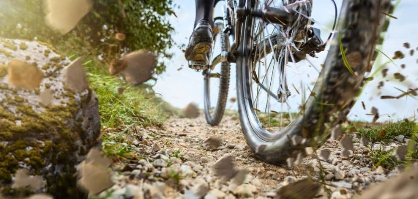 Close-up of bike wheels on a gravel trail, kicking up dust and debris.