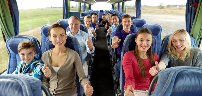 A group of smiling people on a bus gives thumbs up to the camera.