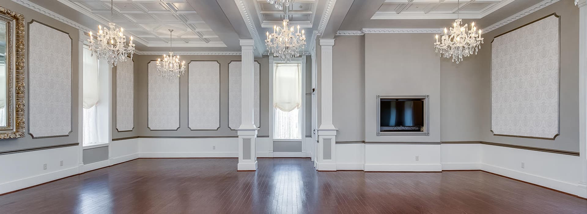 A spacious, elegantly designed room featuring chandeliers, a large mirror, and decorative wall panels.