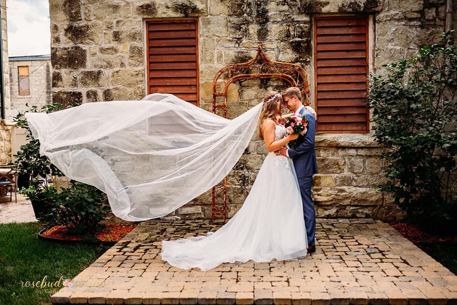 A bride and groom embrace under a flowing veil in a charming outdoor setting.