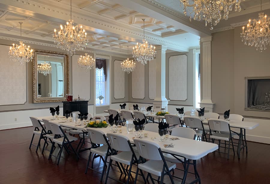 An elegantly arranged dining room with white tables, black napkins, and crystal chandeliers.