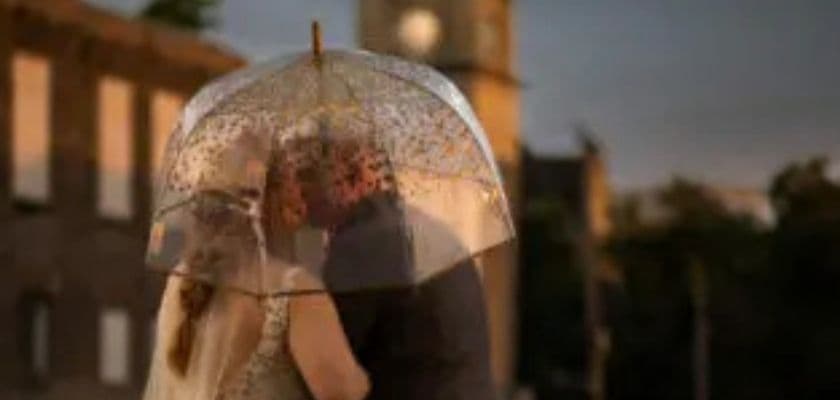 A couple kisses under a clear umbrella during sunset.