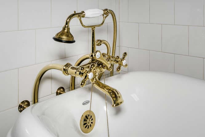 A vintage brass bathtub faucet with a hand shower attachment.