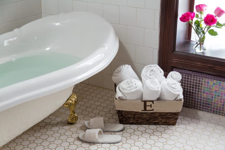 A cozy bathroom featuring a clawfoot bathtub, neatly rolled towels in a basket, and pink roses by the window.