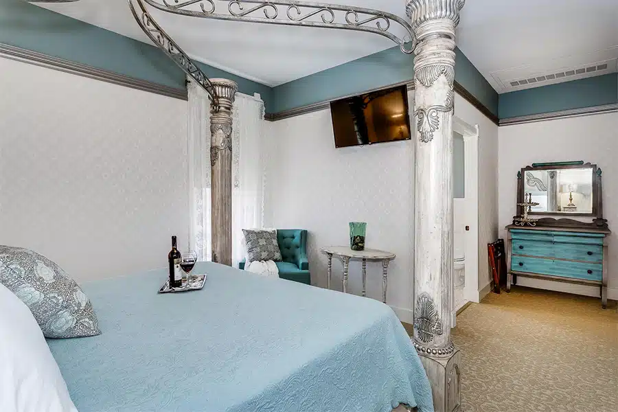A elegantly decorated bedroom featuring a four-poster bed, a television, and vintage furniture.