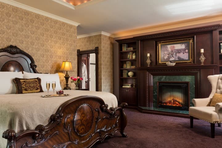 Luxurious bedroom featuring an ornate bed, elegant armchair, and a cozy fireplace.