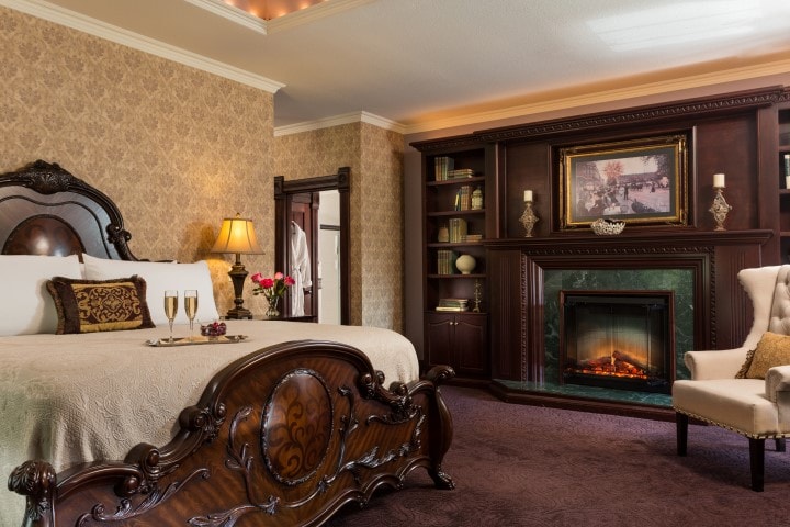 Luxurious bedroom featuring an ornate bed, elegant armchair, and a cozy fireplace.