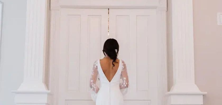 A bride in a white dress stands with her back to the camera, facing a set of ornate double doors.