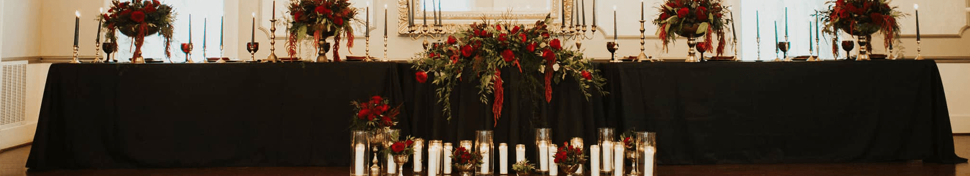 A beautifully decorated table with red floral arrangements and candles, set for a formal event.
