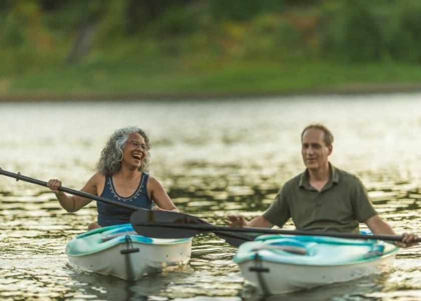 Two people kayaking on a calm lake, smiling and enjoying their time together.