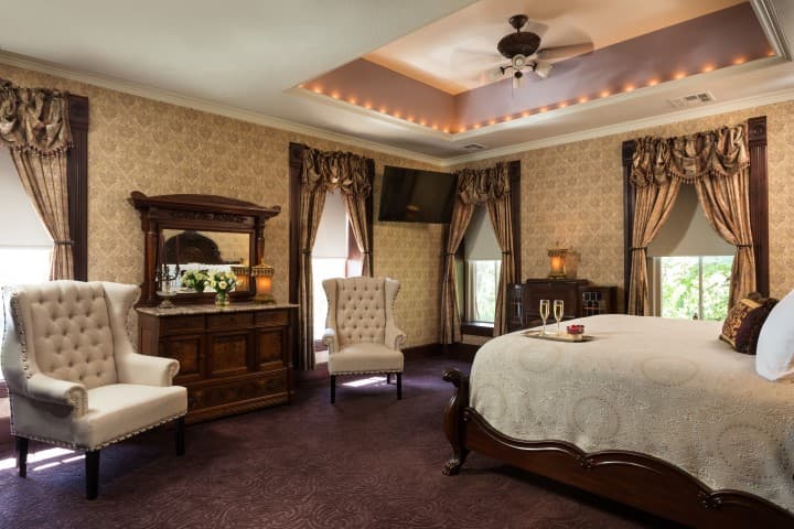 A luxurious bedroom featuring a king-sized bed, elegant chairs, and ornate decor.