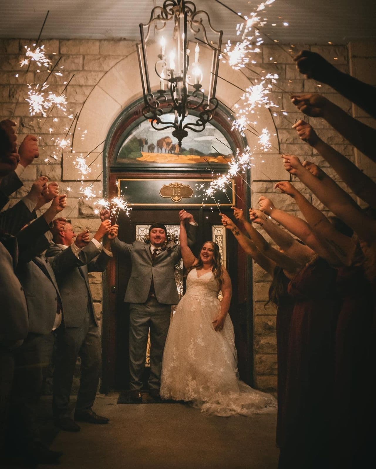 A bride and groom celebrate their wedding as guests hold sparklers in an archway.