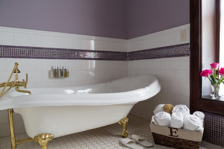 A luxurious clawfoot bathtub surrounded by stylish decor, towels, and fresh flowers.