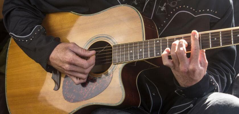 a man wearing western-style shirt and playing an acoustic guitar