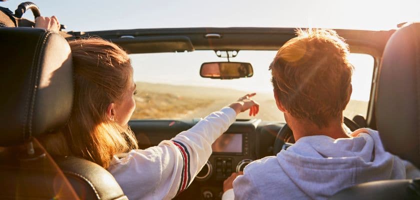 A couple riding in a convertible with the top down, looking out toward a scenic countryside landscape.