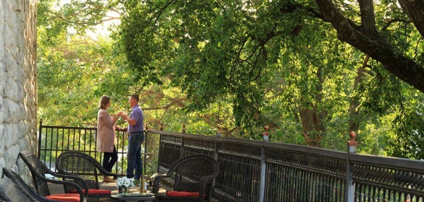 a romantic couple toasting wine on the terrace at the historic elgin hotel in marion kansas surrounded by lush green foliage